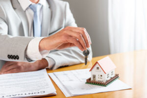 A sales person handing over a key with tiny house on table - What are closing costs